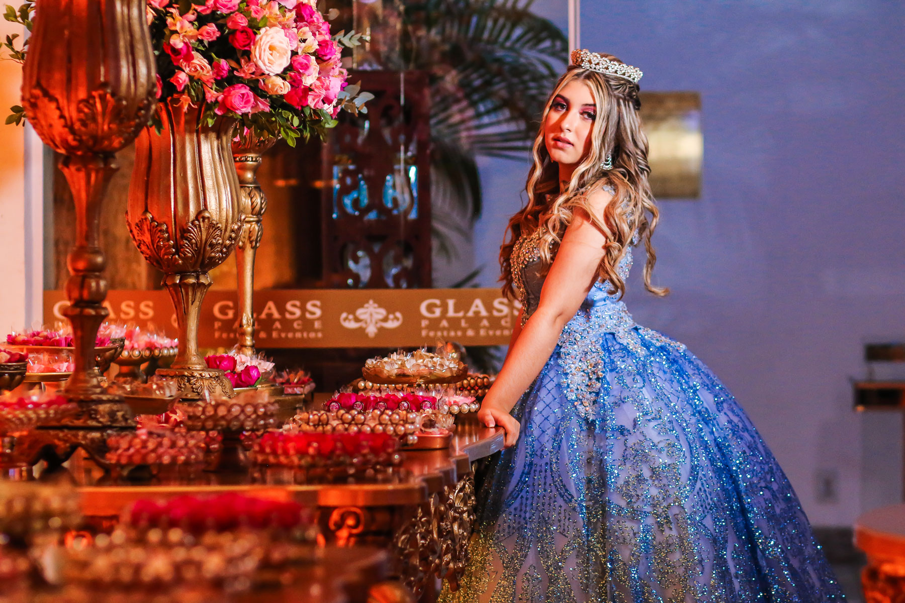 Menina de 15 anos apoiada na mesa decorada com vestido azul no Glass Palace Festas & Eventos