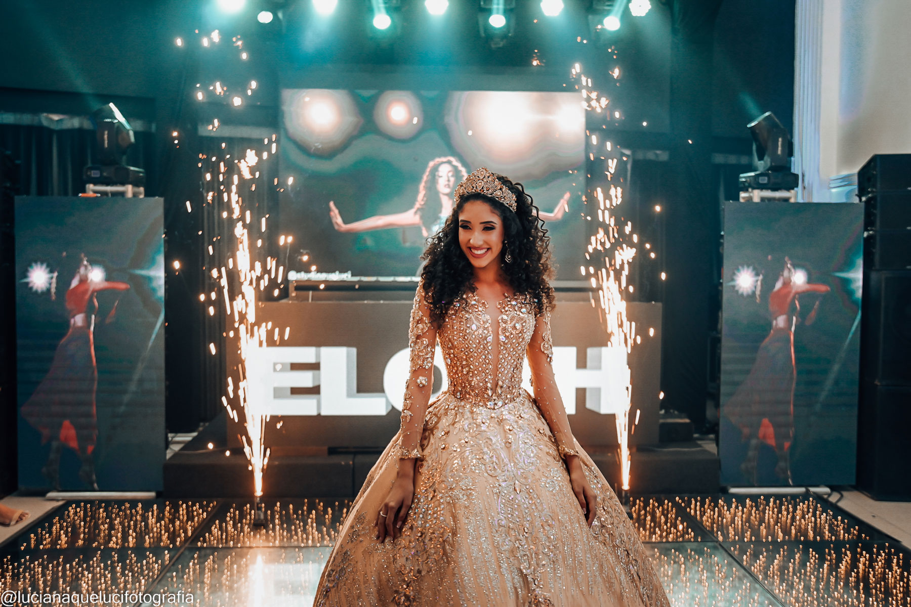 Debutante com vestido dourado e coroa de princesa na pista de dance fazendo pose para a foto