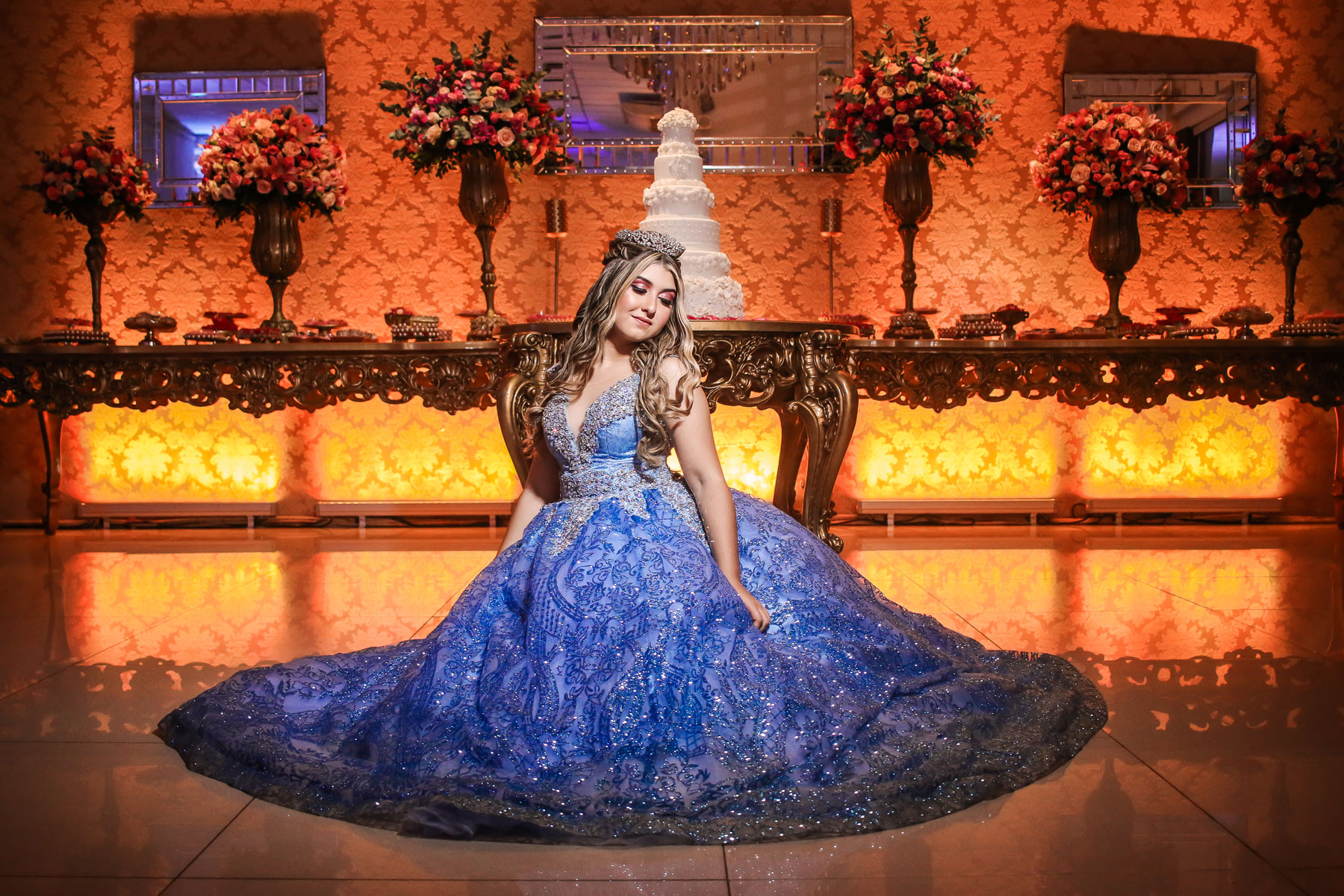 Debutante com vestido azul e coroa de princesa em frente a mesa do bolo